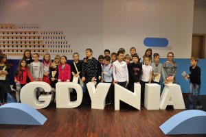 Grupa dzieci stoi za dużym napisem "Gdynia"