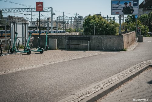 widok na chodnik i ścieżkę rowerową, widoczne zaparkowane hulajnogi oraz ławka