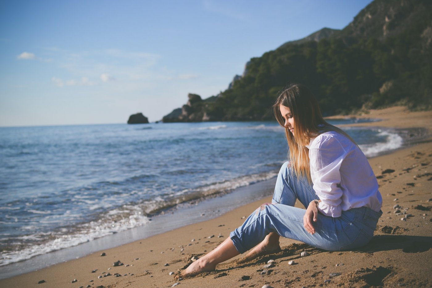 Młoda kobieta siedząca w ubraniu na plaży. Zdj. ilustracyjne // unsplash.com