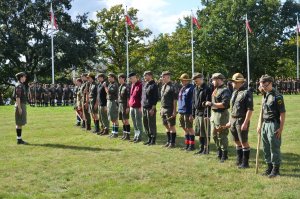 Grupa harcerzy w mundurach i bluzach stojąca na polanie