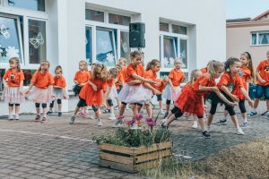 Tańczące przed budynkiem dzieci w czerwonych strojach