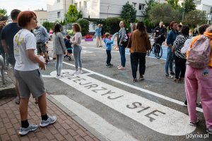 Jeden z napisów na pierwszej ulicy szkolnej w Gdyni i stojąca przy nim grupa ludzi