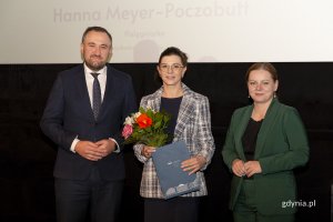 Laureat konkursu z kwiatami i dyplomem pozuje do zdjęcia z Prezydent Miasta Gdyni i dyrektorem zarządzającym 