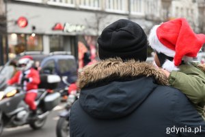 Tata z dzieckiem na rękach obserwuje paradę mikołajów na motocyklach