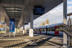 Peron na stacji kolejowej, na która wjeżdża pociąg.