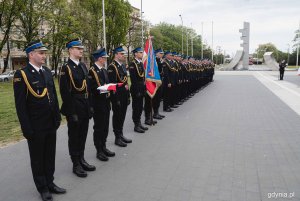 Strażacy stoją w szeregu na placu miejskim.