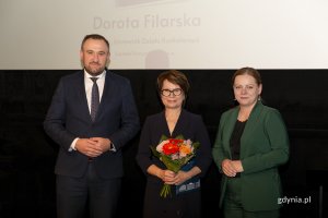 Laureat konkursu z kwiatami i dyplomem pozuje do zdjęcia z Prezydent Miasta Gdyni i dyrektorem zarządzającym 