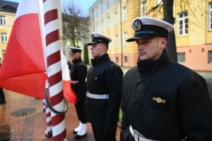 Trzej mężczyźni w mundurach stoją na baczność przy maszcie z Flagą Polski