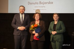 Laureat konkursu z kwiatami i dyplomem pozuje do zdjęcia z Prezydent Miasta Gdyni i dyrektorem zarządzającym 