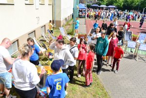 Grupka rodziców przy wielkich kotłach pełnych lemoniady z kawałkami owoców, kolejka dzieci czekająca na napój