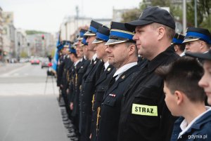 Strażacy stoją w szeregu na placu miejskim.