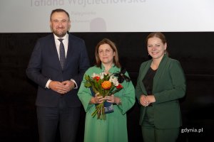 Laureat konkursu z kwiatami i dyplomem pozuje do zdjęcia z Prezydent Miasta Gdyni i dyrektorem zarządzającym 