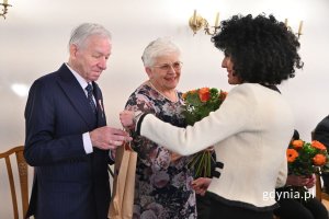 Inocenta Nycz wręczająca parze seniorów pomarańczowy bukiet kwiatów