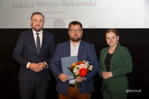 Laureat konkursu z kwiatami i dyplomem pozuje do zdjęcia z Prezydent Miasta Gdyni i dyrektorem zarządzającym 