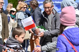 Polityk rozdaje dzieciom chorągiewki Polski.