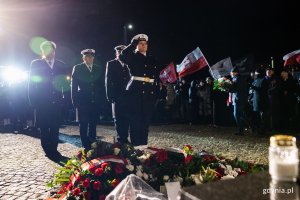 Żołnierze Marynarki Wojennej składają kwiaty pod pomnikiem, w tle zgromadzony tłum