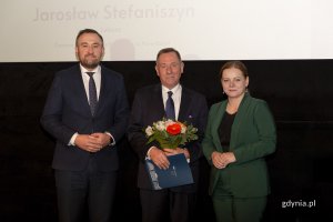 Laureat konkursu z kwiatami i dyplomem pozuje do zdjęcia z Prezydent Miasta Gdyni i dyrektorem zarządzającym 