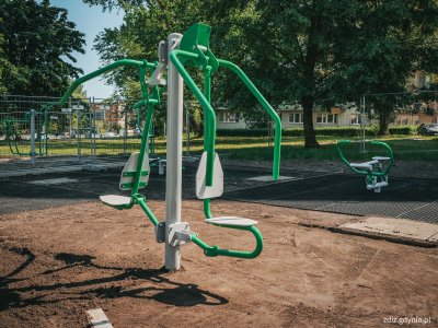 na pierwszym planie urządzenie siłowni zewnętrznej, w tle prace budowlane, widoczne ogrodzenie