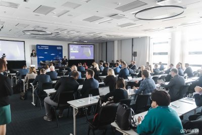 Sala konferencyjna w hotelu Courtyard by Marriott. Widownia na sali. Na scenie kilka osób podczas panelu dyskusyjnego, ścianki z logotypem Transport Week