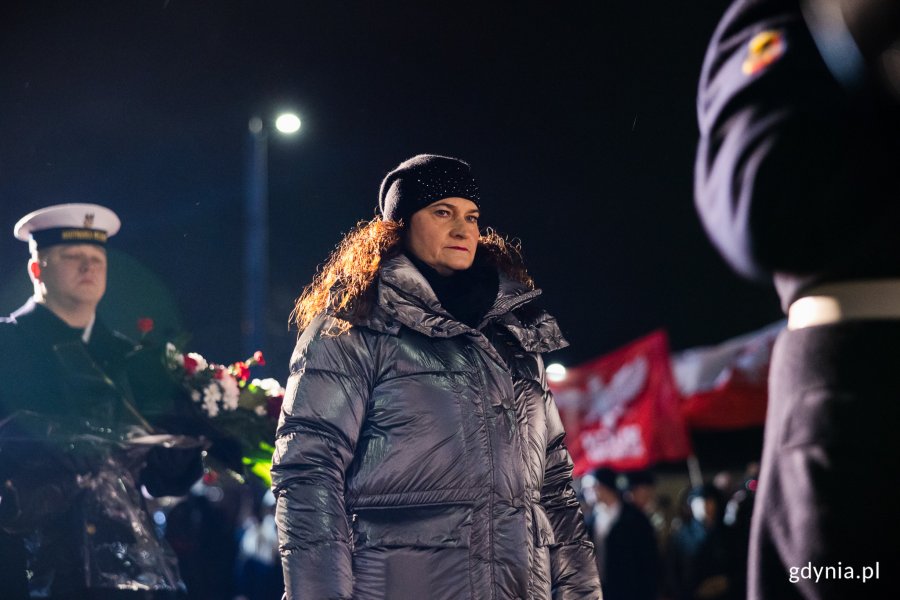 Kobieta oddaje hołd pod pomnikiem, w tle żołnierz Marynarki Wojennej z wieńcem kwiatów