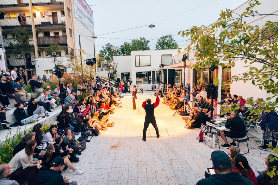 Aktorzy Teatru Ósmego Dnia i publiczność zgromadzona na patio Przystani Widna 2A podczas pokazu spektaklu  „Kapral w Kościółku” w ramach „Pociągu do Miasta”