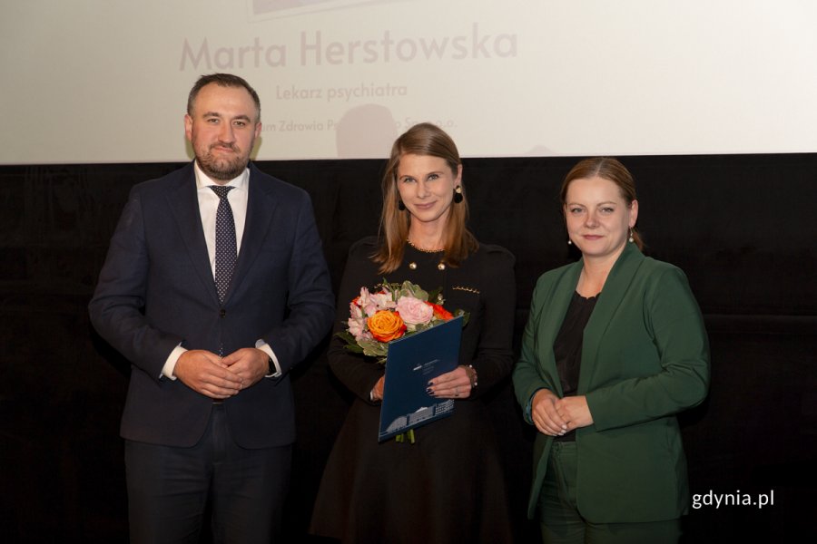 Laureat konkursu z kwiatami i dyplomem pozuje do zdjęcia z Prezydent Miasta Gdyni i dyrektorem zarządzającym 