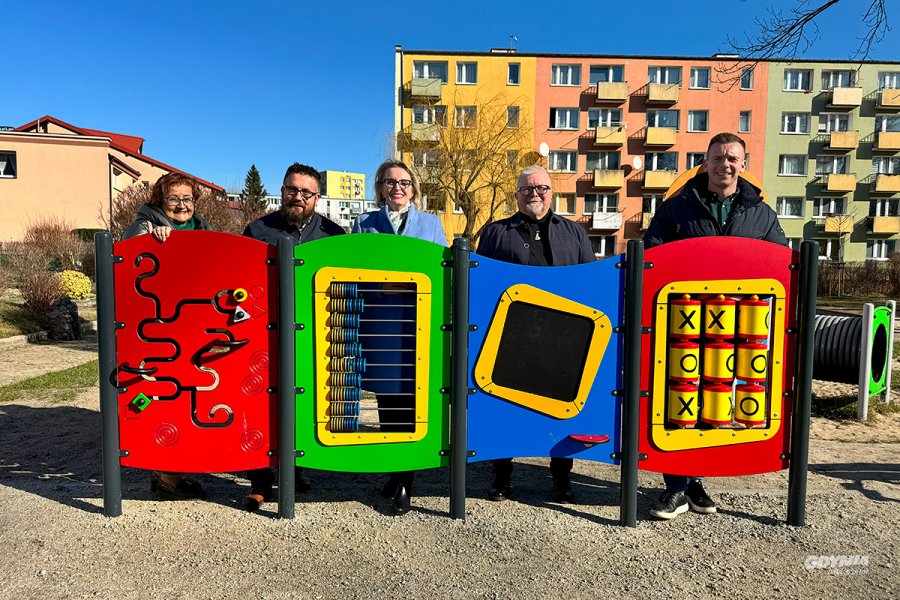 Uczestnicy prezentacji przedszkola stojący przy urządzeniu zabawowym na placu zabaw