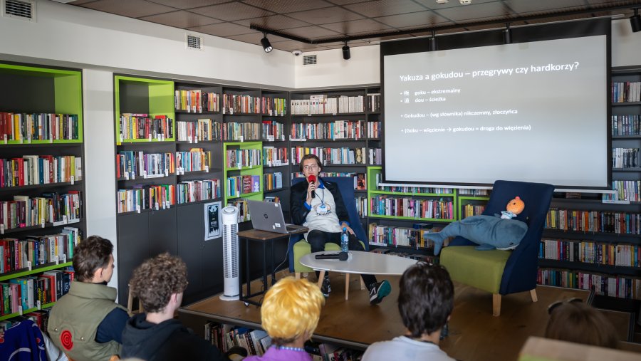 Panel dyskusyjny, w sali biblioteki siedzi prowadzący i słuchacze