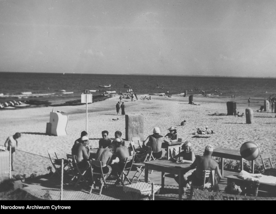 Ludzie siedzący przy dużych stołach na plaży, w tle morze