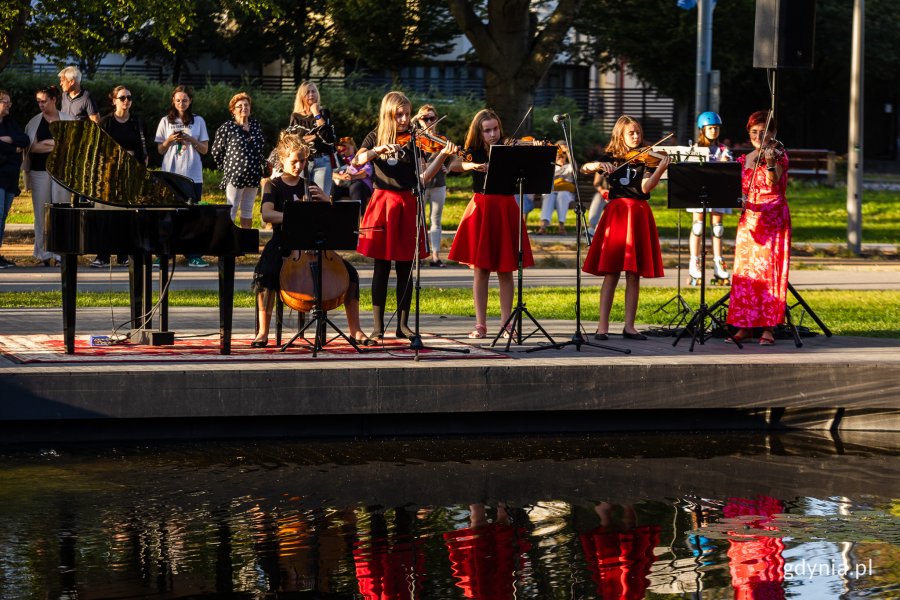 Uczniowie grają na różnych instrumentach nad stawem w parku.