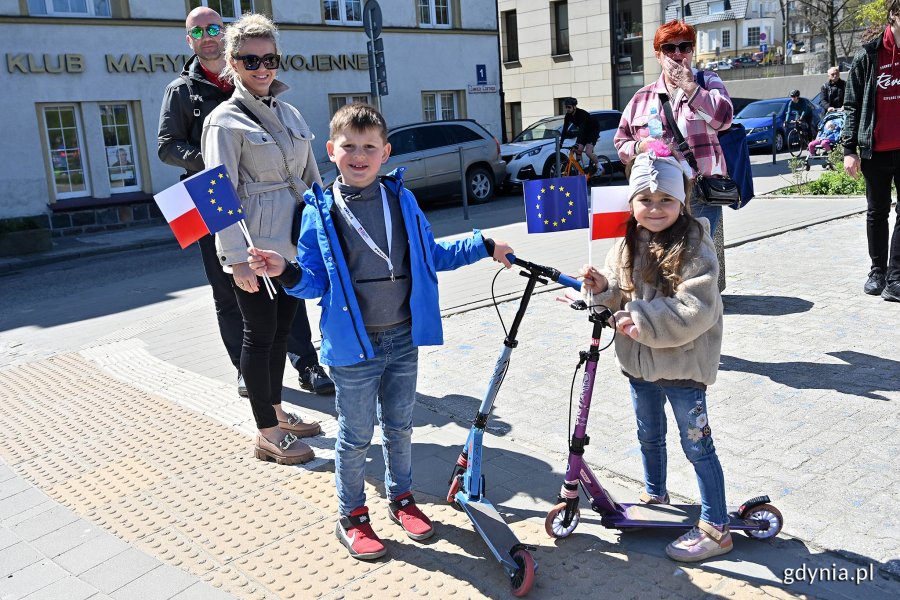 Dzieci z rodzicami trzymają chorągiewki Polski i Unii Europejskiej.