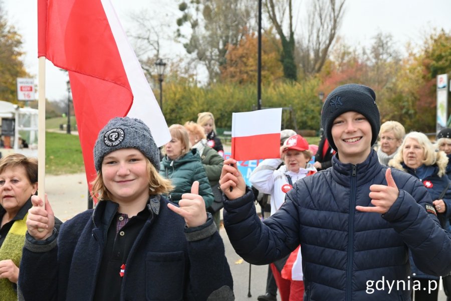 Uczniowie idący w paradzie ulicą Orłowską, trzymają polskie flagi