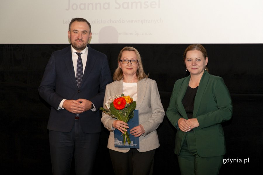 Laureat konkursu z kwiatami i dyplomem pozuje do zdjęcia z Prezydent Miasta Gdyni i dyrektorem zarządzającym 