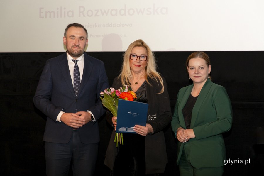 Laureat konkursu z kwiatami i dyplomem pozuje do zdjęcia z Prezydent Miasta Gdyni i dyrektorem zarządzającym 