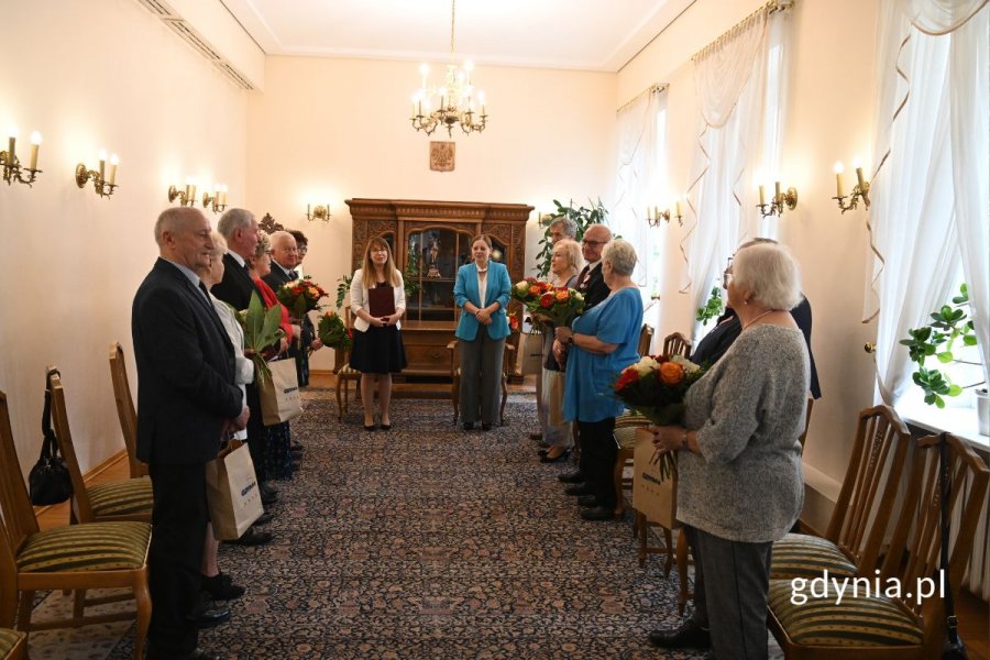 Grupa seniorów stojących w eleganckiej sali