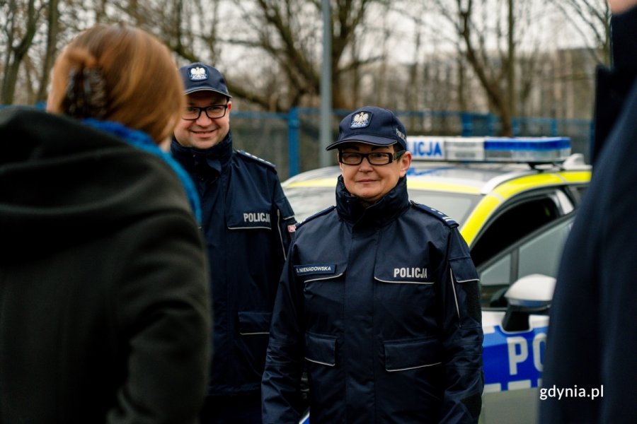 Dwoje funkcjonariuszy policji w mundurach na tle radiowozów