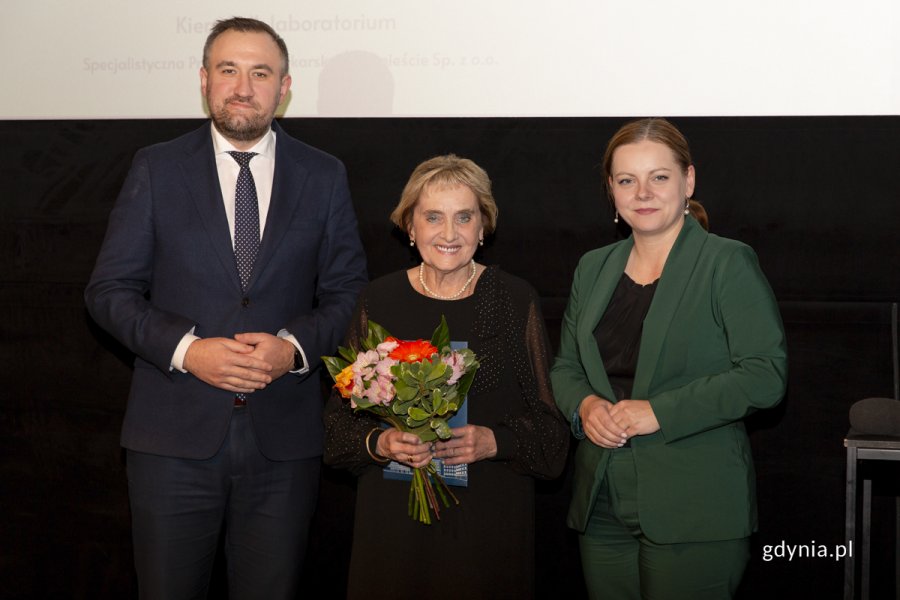 Laureat konkursu z kwiatami i dyplomem pozuje do zdjęcia z Prezydent Miasta Gdyni i dyrektorem zarządzającym 