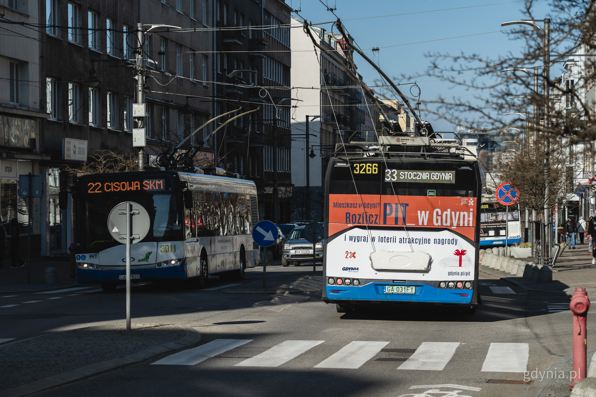 Ulica Świętojańska, dzień, jezdnia, budynki, na środku dwa trolejbusy, na jednym reklama Rozlicz PIT w Gdyni