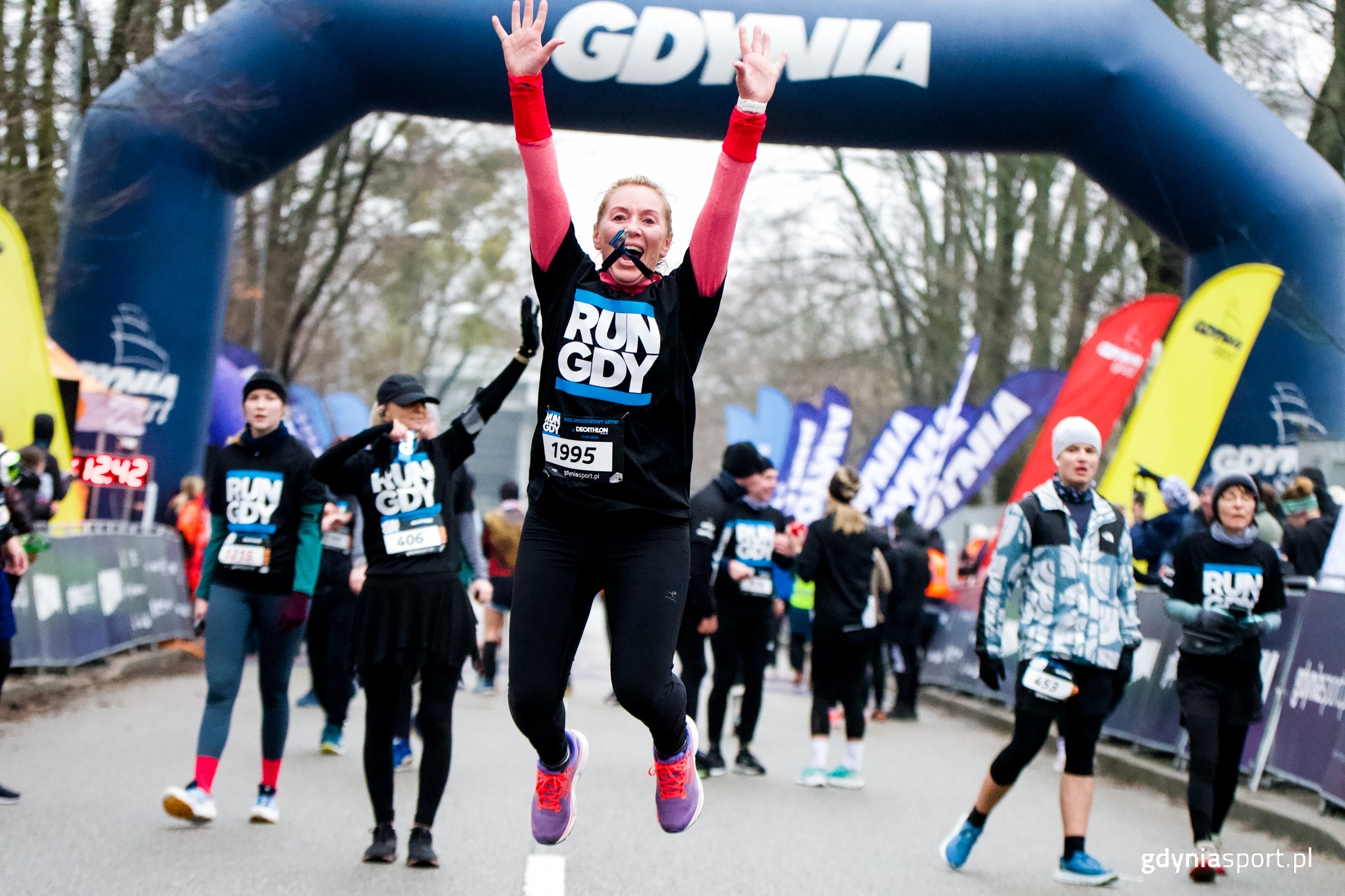 Uśmiechnięta, skacząca kobieta na mecie Biegu Urodzinowego Gdyni z Decathlon