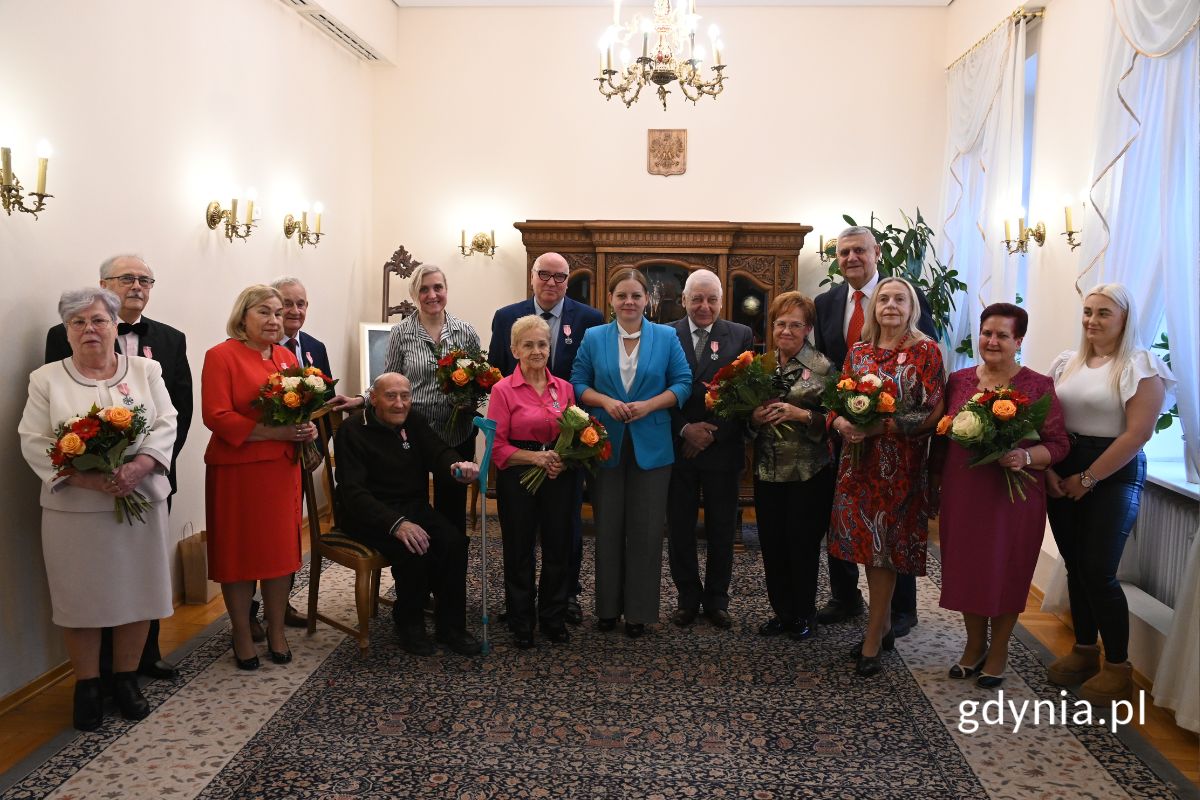 Grupa seniorów stojąca w rzędzie z prezydent Gdyni Aleksandrą Kosiorek