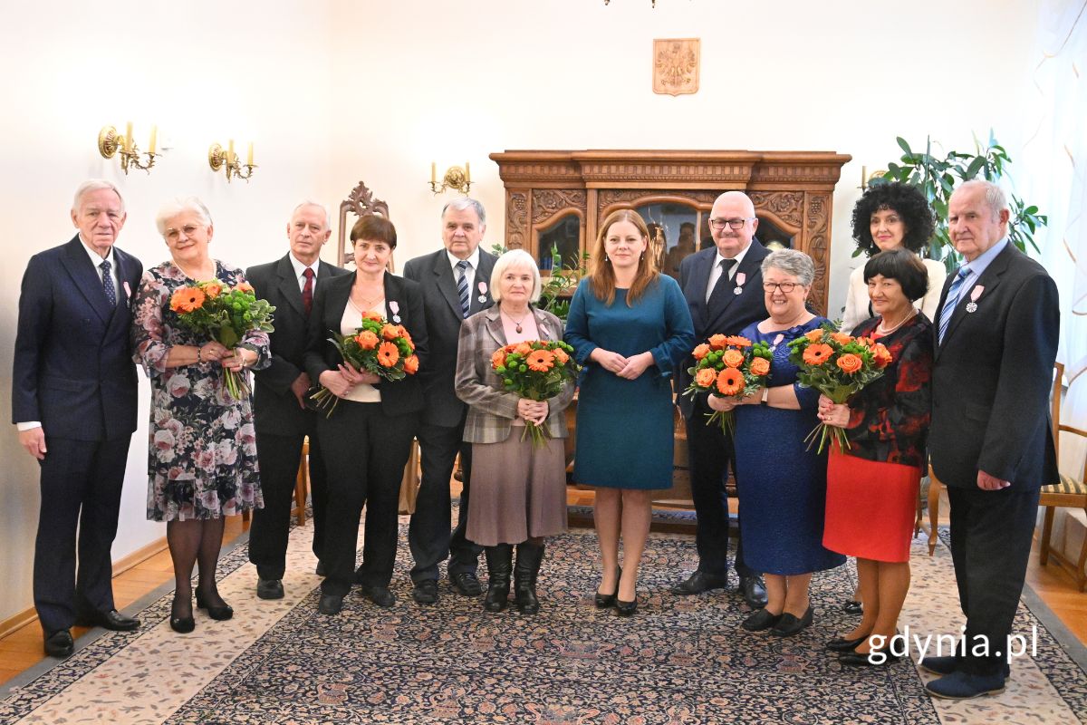 Seniorzy stojący w eleganckiej sali z Aleksandrą Kosiorek i Inocentą Nycz